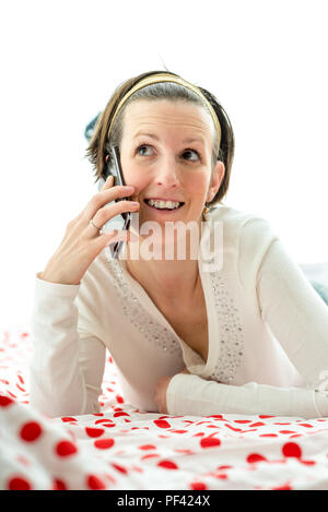 Fröhliche junge Frau bequem auf Ihr Bett in ein angenehmes Gespräch am Handy. Stockfoto