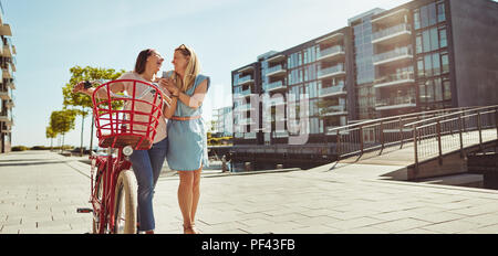 Zwei besten Freunden Spaß haben und Lachen beim zusammen zu Fuß mit dem Fahrrad durch die Stadt im Sommer Stockfoto