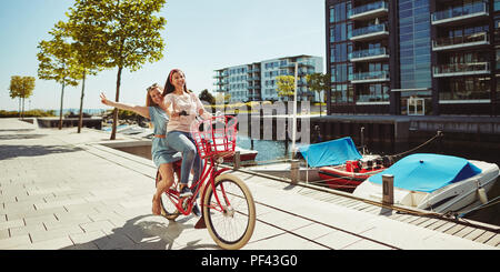 Lächelnden jungen Frau und ihr Lachen Freund reiten durch die Stadt zusammen mit dem Fahrrad im Sommer Stockfoto