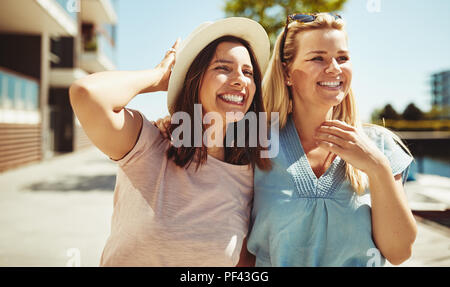 Zwei lachende Junge weibliche Freunde haben zusammen eine gute Zeit zu Fuß an einem sonnigen Tag in der Stadt Stockfoto