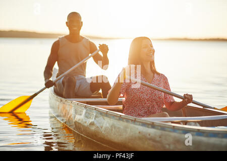 Lächelnde junge Frau und ihre boyfrind paddeln Kanu zusammen auf einem See an einem sonnigen Nachmittag Stockfoto