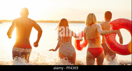 Rückspiegel der Gruppe von jungen Freunde in Badebekleidung in einen See zusammen laufen bei Sonnenuntergang Spritzwasser. Stockfoto