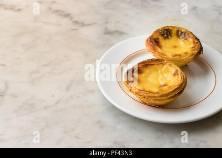 Zwei Pastel de Nata, eine portugiesische traditionelle Dessert auf einer weißen Platte über einen Marmorboden Spachtel. Stockfoto