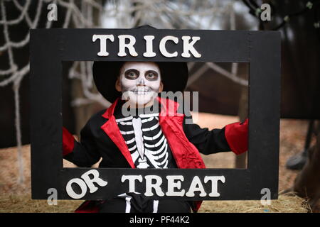 Ein Junge in einem Halloween kostüm Skelett mit Hut und Rauchen hält einen Frame 'Trick or Treat' Stockfoto