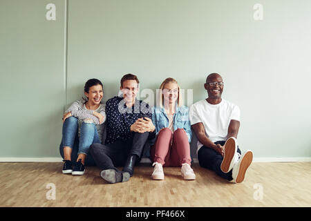 Vielfältige Gruppe junger Geschäftsleute Lachen beim zusammen sitzen auf dem Boden eines Büros während ihrer Pause Stockfoto