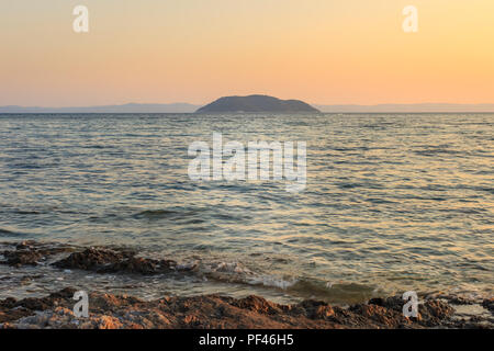 Vordergrund Felsen und welliges Meer vor der Turtle Island in Griechenland bei Sonnenuntergang, gesehen vom Riff am Strand in Neos Marmaras Paradaisos Stockfoto