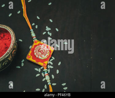 Rakhi mit Reis Körner, kumkum mit Holz- Hintergrund und mit eleganten Rakhi. Ein traditionelles indisches Armband. Stockfoto