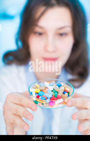 Junge Frau Doktor lächelnd und eine Pille auf blauem Hintergrund Holding Stockfoto