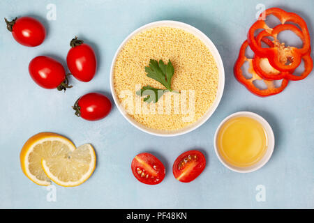 Rohes Couscous und Gemüse zum Kochen auf einem blauen Hintergrund. Ansicht von oben Stockfoto