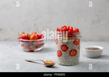 Gesundes Frühstück. Übernachtung Haferflocken mit Erdbeeren, Chia Samen in einem Glas auf grauem Hintergrund Stockfoto