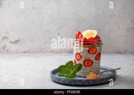 Gesundes Frühstück. Übernachtung Haferflocken mit Erdbeeren, Chia Samen in einem Glas auf grauem Hintergrund Stockfoto