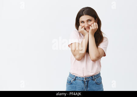 Dumme niedlichen europäischen Freundin mit braunen Haaren in trendigem Pink t-shirt breit grinsend und schiefen Gesicht auf Fäusten während neugierig Zuhören zu attraktiven Freund erzählen interessante Geschichte während Datum Stockfoto