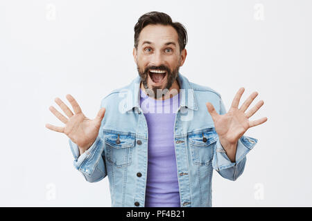 Buh. Charmante sorglos und glücklich nach Kerl mit Bart und Schnurrbart in Jeans Jacke über t-shirt, die Handflächen hoch wie erschrecken, wenn Er wünscht, jemand oder gestikuliert während amüsante Rede, die Zahl Zehn Stockfoto