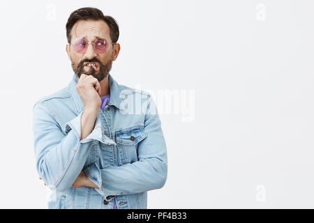 Mann haftete mit schwierige Wahl. Nervös und ängstlich stattlichen reifer Kerl in der Sonnenbrille und Jeansjacke umgekippt, Beißen, Lippe und runzelte die Stirn während sie ihren Blick mit besorgten Blick beiseite, denke, wie Problem lösen Stockfoto