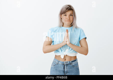 Bitte, hilf mir, Freund. Portrait von intensiven cute Europäische weibliche Mitarbeiter in modischer 7/8-top mit Bauch löchrig, Holding hands in beten und schürzte die Lippen beim Betteln oder sich entschuldigen Stockfoto