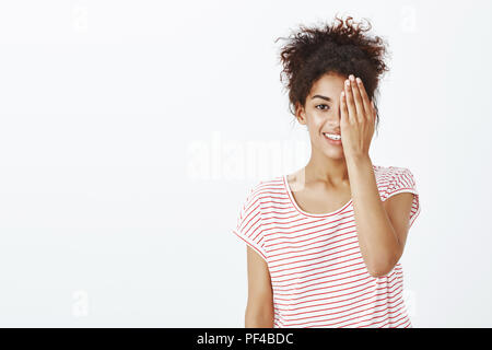 Mädchen tun Make-up zeigt Vor und Nach. Portrait von positiven Süße dunkelhäutige Frau in gestreiften T-Shirt, die halbe Gesicht und breit grinsend beim Prüfen der Vision Optiker Büro Stockfoto