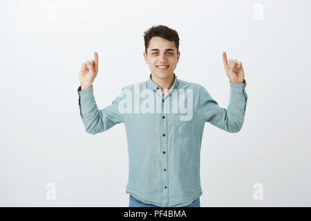 Portrait von Sorglos gut aussehender junger Mann in casual Outfit, Zeigefinger und nach oben zeigend, breit grinsend, die gemeinsame Nutzung großer Platz für Werbung oder Wegbeschreibungen auf Fremde auf der Straße Stockfoto