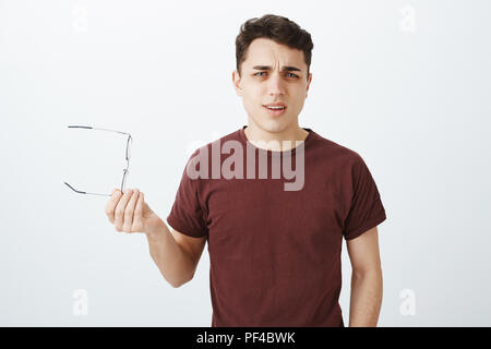 Was ist Ihr Punkt. Portrait von frustriert, verärgert stattlichen erwachsenen Mann im roten T-Shirt, Brille und Sie winken in der Hand, heben auf die Augenbraue und in die Kamera starrt über graue Wand enttäuscht Stockfoto