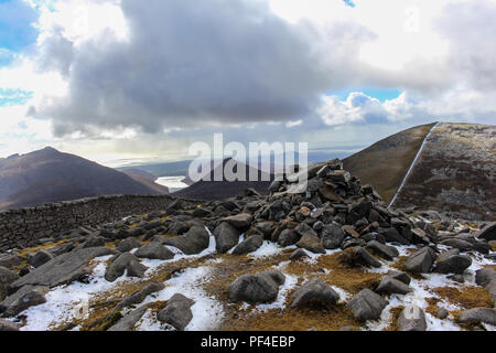 Slieve Meelmore Gipfel Cairn mit leichtem Schneefall. Doan moutain und Silent Valley Reservoir in der Entfernung. Mourne Mountains, N. Irland. Stockfoto