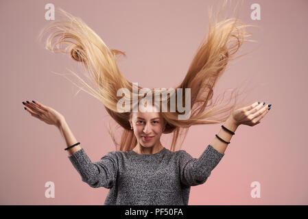 Frau mit fliegenden Haaren auf rosa Hintergrund. Lange blonde Haare Stockfoto