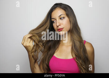 Attraktive junge Frau, die ihr langes Haar. Schöne Mädchen schaut besorgt/an den Spitzen der Haare auf grauem Hintergrund zufrieden. Stockfoto