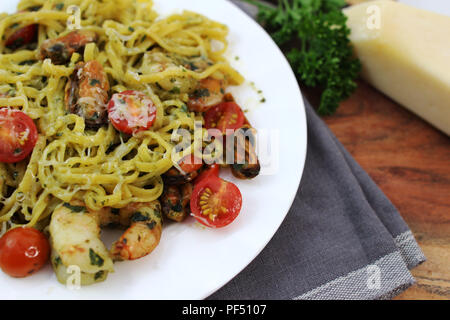 Pesto Linguine mit Tomaten, Garnelen und Muscheln auf einer weißen Platte. Stockfoto