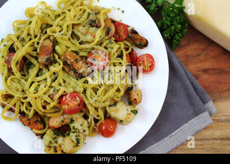 Pesto Linguine mit Tomaten, Garnelen und Muscheln auf einer weißen Platte. Ansicht von oben Stockfoto