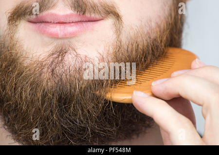 Nahaufnahme eines jungen Mannes styling seinem langen Bart mit einem Kamm, während allein in einem Studio vor einem weißen Hintergrund Stockfoto