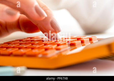 Nahaufnahme der weiblichen Buchhalter oder Banker, die Berechnungen auf orange Tischrechner. Stockfoto