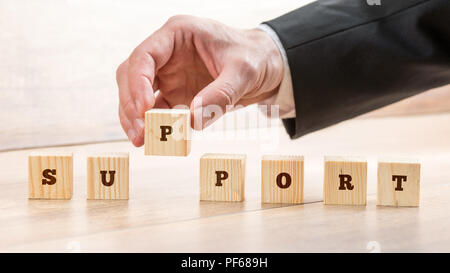 Nahaufnahme der Hand eines Geschäftsmannes arrangieren kleine Holzklötze auf der Tabelle für Business Support und Customer Service Konzept. Stockfoto