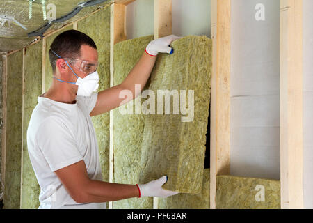 Arbeiter in der Schutzbrille und Atemschutz Dämmstoffe Steinwolle Isolierung in Holzrahmen für die zukunft haus Wände für kalte Barriere. Wohlig warmes Stockfoto