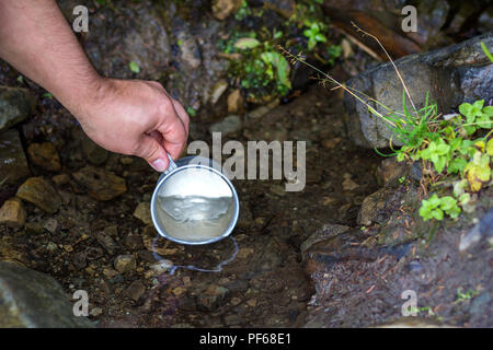 Nahaufnahme der Hand mit touristischen Aluminium Schale scooping saubere, frische süsse Wasser aus natürlichen Mountain Creek für das Trinken. Tourismus, aktiven Lebensstil, n Stockfoto