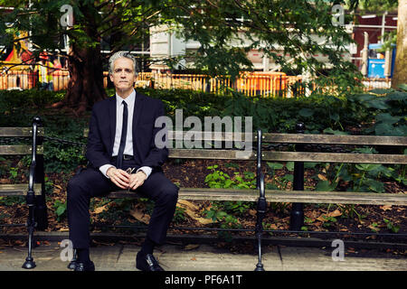 Grauhaariger Mann im schwarzen Anzug sitzt auf einer Parkbank Stockfoto