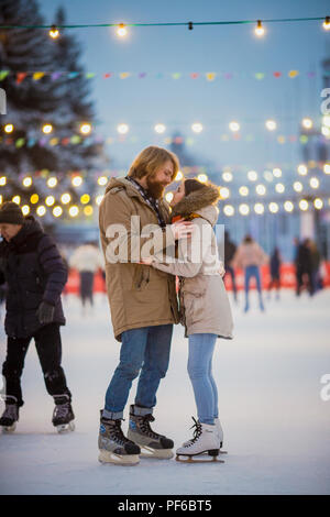 Junges Paar in Liebe kaukasischen Mann mit blondem Haar mit langen Haaren und Bart und schöne Frau Spaß haben, aktive Datum Eislaufen Auf dem Eis Arena in Stockfoto