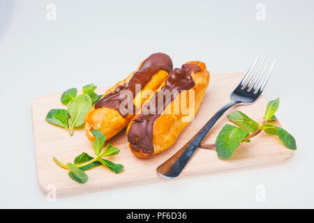 Eclairs auf Platte auf eine Tabelle auf hellen Hintergrund. Pudding Kuchen, Eclair mit Schokolade und Sahne Dessert auf einer Holzplatte, weißer Hintergrund, mint Stockfoto