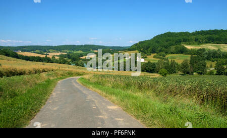 Eine Landstraße schlängelt sich durch die hügelige Landschaft in der Nähe von frespech an einem sonnigen Nachmittag Anfang Sommer in ländlichen Lot-et-Garonne, Frankreich Stockfoto
