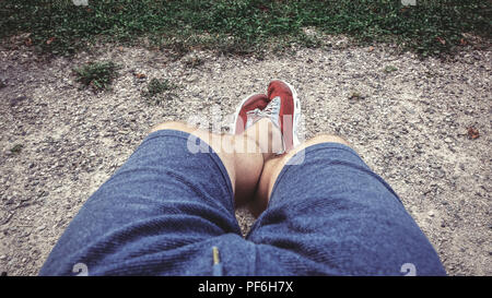 Die Beine eines sitzenden Mann in Shorts und Turnschuhen. Blick von oben. Stockfoto