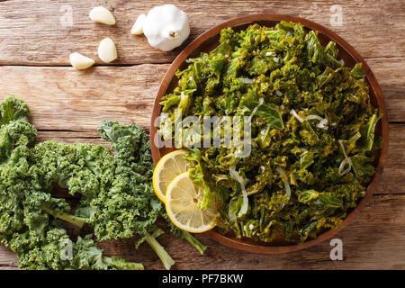 Kale blatt Eintopf mit Zwiebeln, Knoblauch, Olivenöl und Zitrone close-up auf einem Teller und Zutaten auf den Tisch. Horizontal oben Ansicht von oben Stockfoto