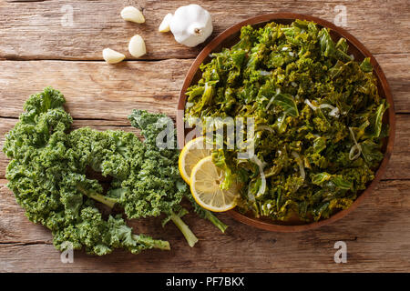 Frisch Grünkohl Kohl mit Zwiebel und Knoblauch und Zitrone close-up auf einem Teller gekocht. Horizontal oben Ansicht von oben Stockfoto