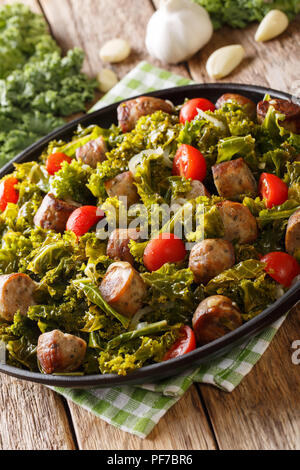 Gebratener Rotkohl Grünkohl mit Wurst, Tomaten und Parmesan auf einer Platte close-up auf dem Tisch. Vertikale Stockfoto