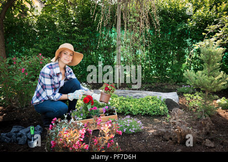 Schöne weibliche Gärtner an Kamera suchen, mit Blumen in Ihrem Garten gepflanzt werden. Gartenarbeit Konzept. Stockfoto