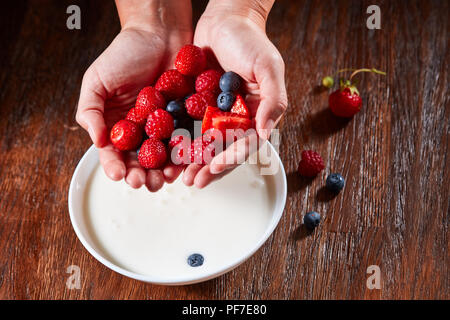 Frische organische Früchte, Erdbeere, Himbeere, Heidelbeere in Mädchen Hände und weiße Schüssel mit Milch auf einem hölzernen Hintergrund, kopieren. Gesunde vegetarische Stockfoto
