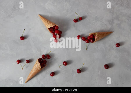 Gesunde reife rote Früchte, Kirsche und Waffel Cups für hausgemachtes Eis auf einem grauen Stein Hintergrund mit Platz für Text. Sommer organischen Essen. Stockfoto