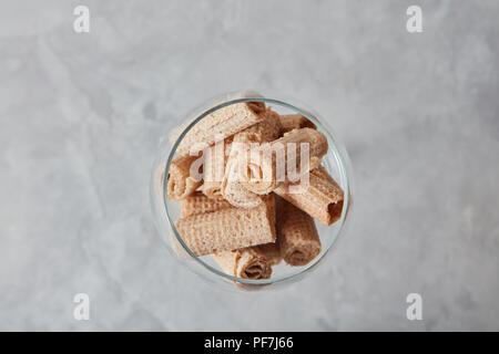 Blick von oben auf die cremige Waffelröllchen in einem Glas Schale Dessert für Wein auf einem grauen Stein Tabelle. Stockfoto