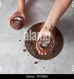 Hausgemachte Schokolade Dessert in einem Coconut shell Holding womans Hände über runde Board auf einem grauen Hintergrund mit Platz für Text. Sommer Nachtisch. Stockfoto
