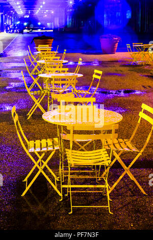 Nicht belegte Gelb - Metall Tische und Stühle in der Regen in der Nacht gemalt, King's Cross, London, UK, 2012 Stockfoto