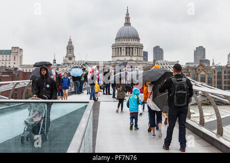 Touristen mit Sonnenschirmen kämpfen blustery Regen auf die Millennium Bridge, London, UK Stockfoto