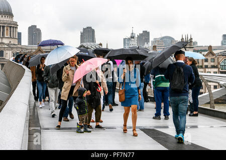 Touristen mit Sonnenschirmen kämpfen blustery Regen auf die Millennium Bridge, London, UK Stockfoto