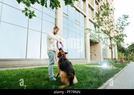 Blonde junge Mann spielt mit Hund in der Nähe von seinem Haus Stockfoto