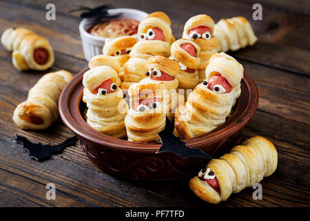 Beängstigend wurst Mumien im Teig mit lustigen Augen auf den Tisch. Lustige Dekoration. Halloween Essen. Stockfoto